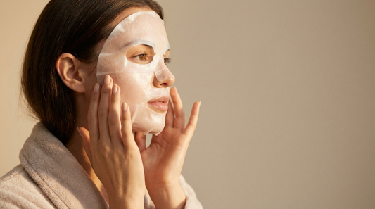 Jeune femme appliquant un masque en tissu sur le visage, fond ivoire et taupe, ambiance clean beauty premium Soveya