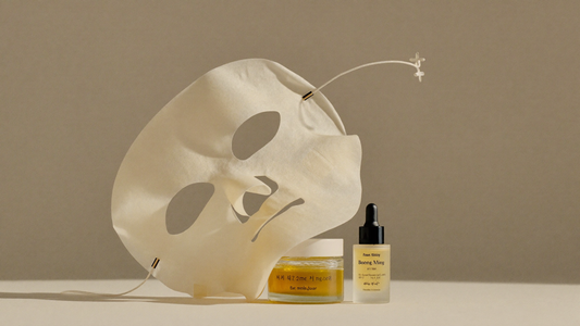 Flat-lay clean beauty d'un masque en tissu coréen et de flacons de skincare sur fond ivoire et taupe
