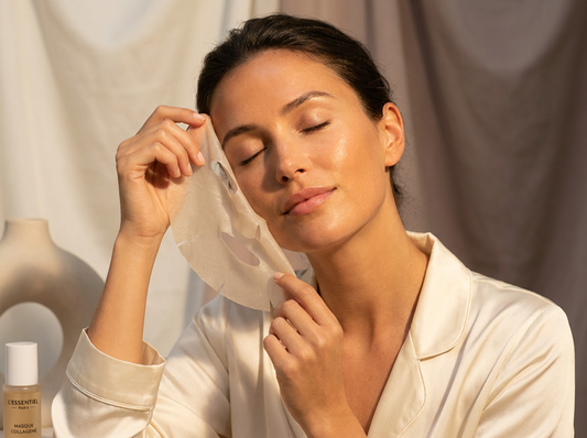 Femme au teint hâlé appliquant un masque tissu coréen au collagène translucide sur son visage, dans une ambiance de studio chaleureuse aux tons ivoire et taupe, esthétique clean beauty premium