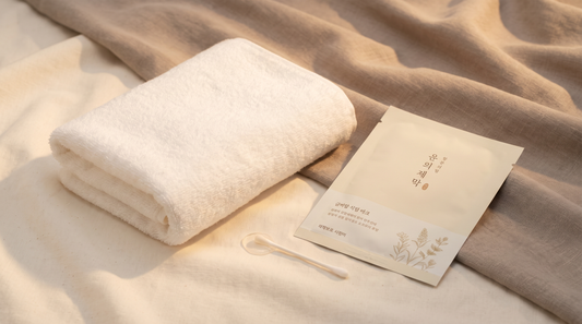 Masque tissu coréen posé sur une serviette blanche, lumière studio chaude, ambiance clean beauty ivoire et taupe